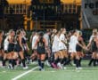 High school field hockey teams greet each other post-match under the stadium lights.