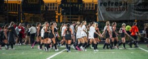 High school field hockey teams greet each other post-match under the stadium lights.