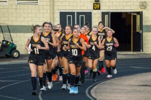 Girls' field hockey team jogging on track, wearing black uniforms. Team spirit and fitness training concept.