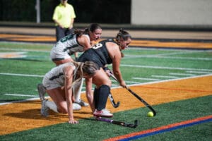 Field hockey players competing intensely for the ball on a green sports field.