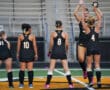 Girls' field hockey team in black uniforms celebrating pre-game on the field.
