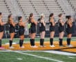 Women's field hockey team lined up in jerseys on a field during a game, preparing for match kickoff.