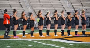 Women's field hockey team lined up in jerseys on a field during a game, preparing for match kickoff.