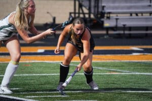 Two female field hockey players competing intensely on a bright green and orange field.