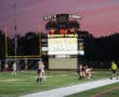 Field hockey match at Wright Field, score 0-1, players in action under the scoreboard at dusk.