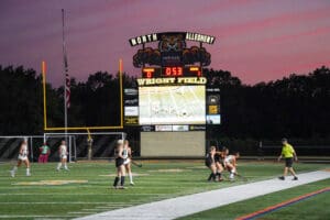 Field hockey match at Wright Field, score 0-1, players in action under the scoreboard at dusk.