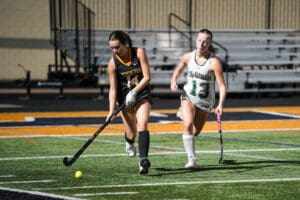 Two female field hockey players competing on a bright field during a match.