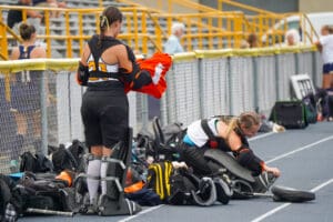Field hockey players preparing gear on the sideline before a match.