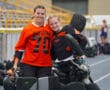Two field hockey goalkeepers in black and orange gear smiling together on the sideline.