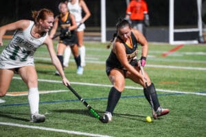 Field hockey players in action during a competitive match, focused on controlling the ball on the field.