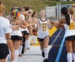High school field hockey players giving high fives before a game, wearing team uniforms on a sports field.