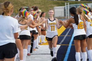 High school field hockey players giving high fives before a game, wearing team uniforms on a sports field.