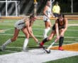 Two field hockey players compete for the ball on a sports field at night.