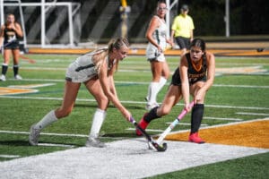 Two field hockey players compete for the ball on a sports field at night.