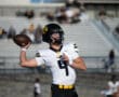 Football player in action, preparing to throw a pass on the field, wearing a black helmet and white jersey.