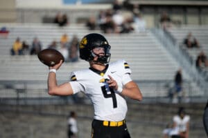 Football player in action, preparing to throw a pass on the field, wearing a black helmet and white jersey.