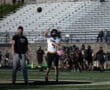 Football player in action throws a pass on the field during practice, with coach observing.