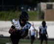 Football player running on field with ball during a game, wearing black and white uniform, helmet, daytime practice.