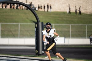 Football player running into the end zone during a game, wearing a black and white uniform and helmet.