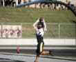 Football player catches touchdown pass in end zone wearing black and yellow uniform, mid-air leap by goalpost.