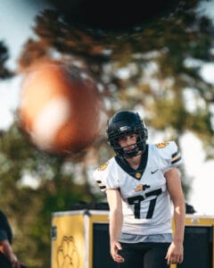 American football player in a helmet observing a moving football during practice outdoors.