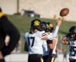 Football players in black and yellow uniforms practicing on the field, one tossing a football in the air.