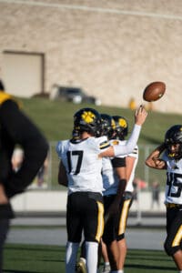 Football players in black and yellow uniforms practicing on the field, one tossing a football in the air.