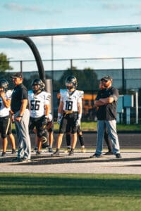 Football team on the sidelines with players and coaches under goalpost during a game.