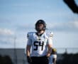 Football player in a helmet and jersey number 54 standing on the field under a clear blue sky.