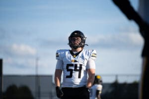 Football player in a helmet and jersey number 54 standing on the field under a clear blue sky.