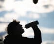 Silhouette of a person drinking water from a bottle against a cloudy sky backdrop.