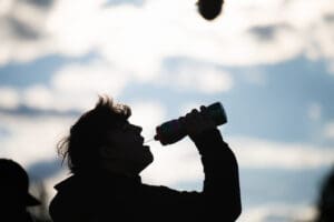 Silhouette of a person drinking water from a bottle against a cloudy sky backdrop.