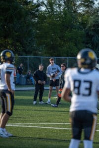 Football players in huddle on field with coaches, discussing strategy during practice session.