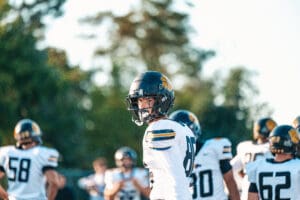 Football player in white jersey and helmet on field with teammates during game.