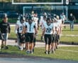 Football team in black uniforms entering field, lined up for game preparation, sunny day.
