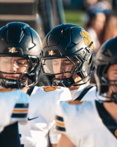 Football players huddled in black helmets and white jerseys during a game, focused and attentive.