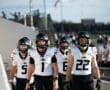 High school football players in black and white uniforms walking onto field, helmets on, ready for the game.