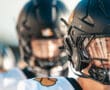 Football players wearing black helmets and white uniforms, focus on determined expression in helmet visor.
