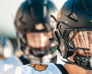 Football players wearing black helmets and white uniforms, focus on determined expression in helmet visor.