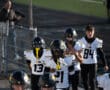 High school football players in black helmets and white jerseys entering the field before a game.