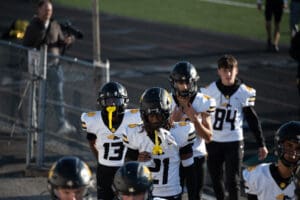 High school football players in black helmets and white jerseys entering the field before a game.