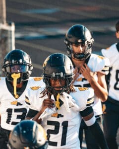 Youth football team in black helmets and white jerseys preparing for a game.