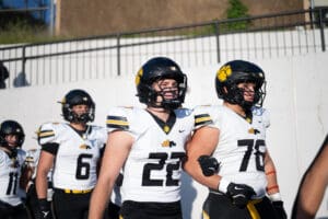 Football players in black and white uniforms walking on the field during a sunny day.
