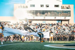 Football players burst through banner on field, energetic game day atmosphere at stadium.