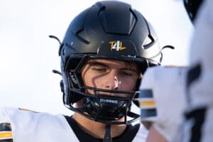 Young football player in black helmet and white jersey focused before the game.