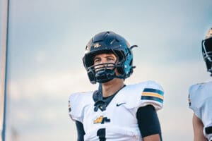 Football player in helmet and uniform looking focused, with a clear sky background.