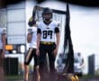Football player in black and white uniform stands on field, ready for game with teammates in background.