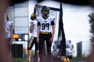 Football player in black and white uniform stands on field, ready for game with teammates in background.