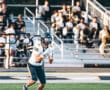 Football player focuses on catching a pass during a high school game, with spectators in the background.