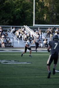 Football player running with the ball during a game, referee in the background.